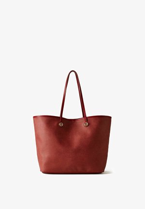 Grande borsa tote in pelle rossa testurizzata con due manici lunghi e ferrature circolari dorate su sfondo bianco.