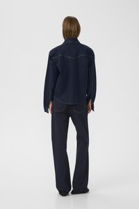 Veste en denim foncé avec épaules tombantes, col pointu et ourlet arrondi, associée à un pantalon en denim foncé à jambes larges avec des coutures visibles.