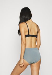 Sutiã preto com alças ajustáveis, combinado com cuecas cinzentas de cintura alta. Ambos os itens apresentam um tecido liso e elástico.