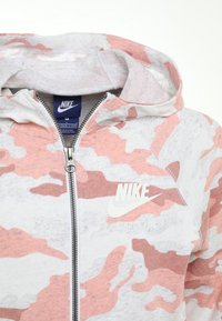 Felpa con zip in un motivo camouflage rosso e bianco, tessuto morbido, dotata di cappuccio, chiusura con zip e presenta il marchio Nike sul petto.
