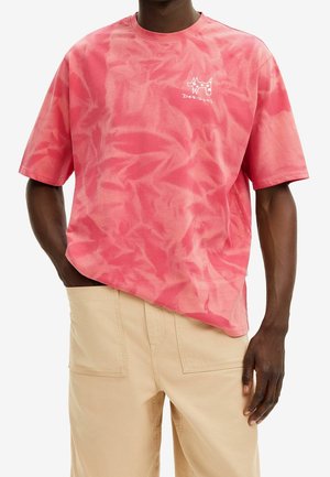 T-shirt en coton surdimensionné tie-dye rose avec des manches courtes et un logo blanc sur la poitrine. Associé à un pantalon beige.