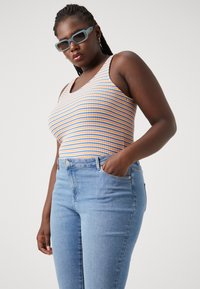 Striped tank top in orange, blue, and yellow; denim jeans; solid color; casual style; model poses with hand in pocket; minimal accessories.