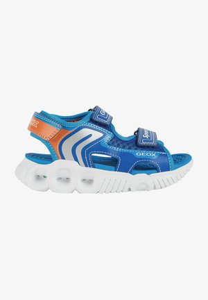 Sandalias deportivas azules con parte superior de malla, suela de goma y tres correas ajustables de velcro. Presenta una suela blanca con orificios circulares y detalles en color naranja.