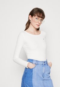 Weißes Langarm-Shirt aus geripptem Stoff mit rundem Ausschnitt, kombiniert mit einem hellblauen Jeansrock mit zweifarbiger Gestaltung und Taschen.