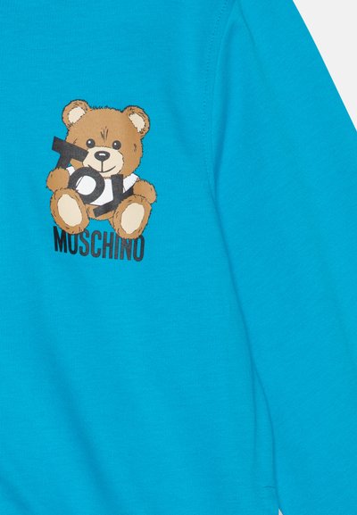 Sudadera turquesa con un gráfico de un oso de peluche marrón sosteniendo un cartel negro que dice "TOY" con el texto "MOSCHINO" debajo. Tejido de algodón suave.