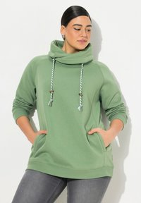 Felpa verde con collo a imbuto, cordini bianchi e verdi, tasche frontali e polsini a costine. Tessuto morbido con una texture liscia.