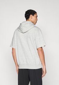 Γκρι κοντομάνικο φούτερ με κουκούλα ρυθμιζόμενη, ριμπ μανσέτες και χαλαρή εφαρμογή. Κατασκευασμένο από απαλό ύφασμα, απεικονίζεται από πίσω.