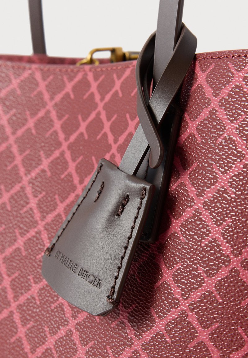 Burgunderfarbene Handtasche mit strukturierter Oberfläche, die ein geometrisches Muster aufweist, dunkelbraune Lederakzente und ein Markenlederetikett.