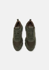 Sneaker verdi con una combinazione di materiali in mesh e suede, punta arrotondata, suola spessa e linguetta posteriore. Design con lacci.