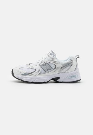 Witte sportieve sneakers met mesh en synthetische overlays, voorzien van een gewatteerde zool, grijze accenten en een logo op de zijkant.