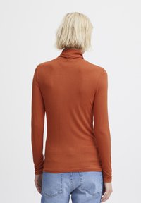 Langärmliges Rollkragenoberteil aus rostfarbener Stoff; figurbetontes Design, weiche Textur und schlichte Rückseite ohne Verzierungen oder Muster.