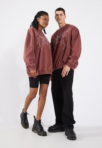 Sudaderas de gran tamaño en color burdeos con diseños gráficos en blanco, combinadas con pantalones cortos de ciclista negros y botas negras con cordones en dos modelos.