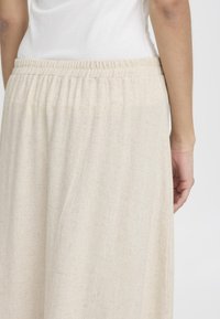 Jupe maxi en coton beige, texturée, avec une taille élastique, suspendue librement, présentée de dos, mettant en avant sa simplicité et sa douceur.