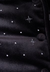 Tessuto di velluto nero con una superficie liscia, decorato con motivi di stelle e punti in filo argentato, e bottoni rivestiti in tessuto nero.