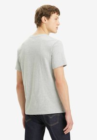 Camiseta gris de manga corta con cuello redondo, fabricada en algodón, con una textura suave, combinada con jeans de mezclilla oscuros que presentan detalles de costura visibles.
