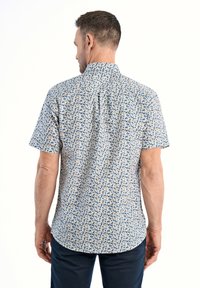 Camicetta a maniche corte di colore bianco con motivo floreale blu e giallo, realizzata in tessuto traspirante. Presenta un colletto standard e un orlo curvo.