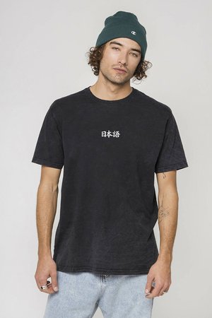 T-shirt in cotone nero con maniche corte, con testo giapponese bianco sul frontale. Indossato con jeans in denim blu chiaro e un berretto verde.