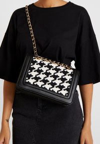 Black and white houndstooth-patterned handbag with a black leather trim and a gold chain strap, featuring a structured rectangular shape.