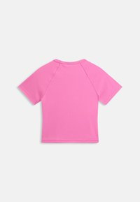 Otrokova roza raglan majica s kratkimi rokavi, položena na ravno površino, z vidnimi šivi na hrbtni strani in okroglim izrezom, na belem ozadju.