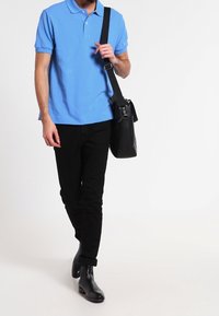 Ljusblå pikétröja med korta ärmar, svarta smala byxor och svarta läderstövlar. En svart axelremsväska bärs över kroppen.