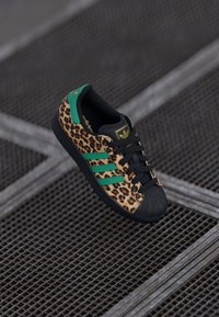 Sneaker con stampa leopardata, punta nera, accenti verdi e lacci neri. Presenta tre strisce verdi e un logo sulla linguetta.