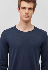 Marineblaues Langarmshirt mit Rundhalsausschnitt, aus glattem Baumwollstoff gefertigt. Es hat eine schlichte Textur mit einem subtilen Nahtdetail am Ausschnitt.