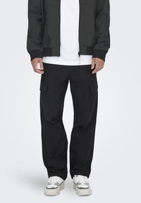 Zwarte cargobroek met meerdere zakken, gemaakt van stevig materiaal, met een losse pasvorm en rechte pijpen. Gevergd met een wit T-shirt en sneakers.