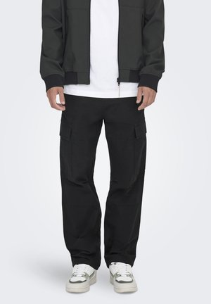 Pantalons cargo noirs avec plusieurs poches, fabriqués en tissu robuste, dotés d'une coupe ample et d'une jambe droite. Portés avec un t-shirt blanc et des baskets.