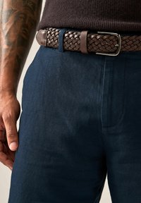 Marineblaue Hose aus strukturiertem Stoff, ausgestattet mit einem gewebten braunen Leder-Gürtel mit einer silbernen Metallschnalle und einer gestickten Einzelheit.