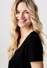 Sort kortærmet skjorte med V-udskæring, lavet af et glat stof, med en afslappet pasform og let stræk, stylet med løse bølgede blonde hår.