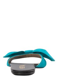Sandalii plate turquoise cu detaliu mare sub forma de fundă, realizați dintr-un material moale asemănător cu suedeul. Talpă neagră cu textură subtilă și branding vizibil.