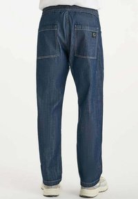 Blauwe denim broek met een relaxte pasvorm, voorzien van twee achterzakken en zichtbare stikseldetails. Elastische tailleband en tapering bij de enkels.