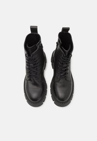 Bottines en cuir noir avec lacets et fermetures éclair sur le côté, dotées d'une épaisse semelle en caoutchouc et d'une finition texturée.