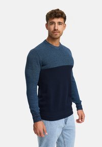 Un pull en maille bleu foncé et bleu clair avec un corps texturé et des manches lisses, doté d'un col rond et d'un ourlet côtelé.