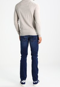 Maglione pullover grigio chiaro con texture a coste, abbinato a jeans aderenti blu scuro e sneakers bianche con accenti blu.
