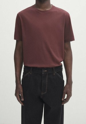 Personne portant un t-shirt bordeaux uni à manches courtes, rentré dans un jean noir taille haute avec des coutures visibles.
