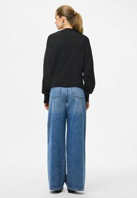 Czarny sweter z okrągłym dekoltem i długimi, lekko bufkami rękawami, w połączeniu z szerokimi, niebieskimi dżinsami z tylnymi kieszeniami.