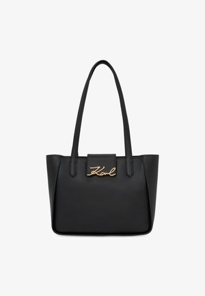 Black leather tote bag with two handles, featuring a structured shape and a gold-tone signature logo on the front. Smooth texture.
