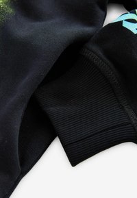Tissu de sweat-shirt noir avec des poignets côtelés. Présente une texture finie et un accent graphique bleu vif. Matière douce et confortable.