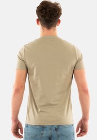 Camiseta beige de manga corta hecha de algodón suave, con un cuello redondo y un corte relajado. Textura suave sin patrones visibles.