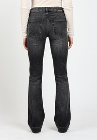 Schwarze Jeans mit ausgestelltem Bein aus Denim mit strukturierter Oberfläche, Fünf-Taschen-Design und gestickten Details auf der Rückseite. Markenlabel am Bund.