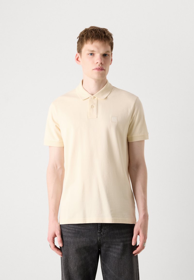 Polohemd in hellgelb, mit kurzen Ärmeln, kragenförmigem Design, ausgestattet mit zwei Knöpfen und einem kleinen Logopatch auf der linken Brust.