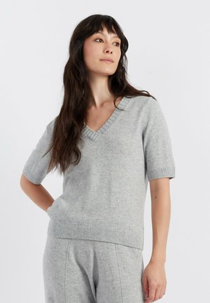 Lichtgrijze gebreide trui met een V-hals, korte mouwen en ribbels aan de manchetten en onderkant. Zachte textuur, comfortabele pasvorm, gecombineerd met bijpassende grijze broek.