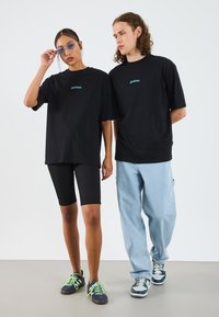 Black oversized t-shirts, ribbed black bike shorts, and casual sneakers with green laces. Unisex, minimalistic design features.
