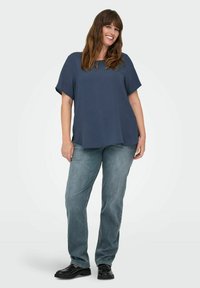 Tamno plava oversized majica kratkih rukava, u kombinaciji sa svijetloplavim ravnimfarmerkama i crnim cipelama; glatkna tkanina, opušteni kroj.