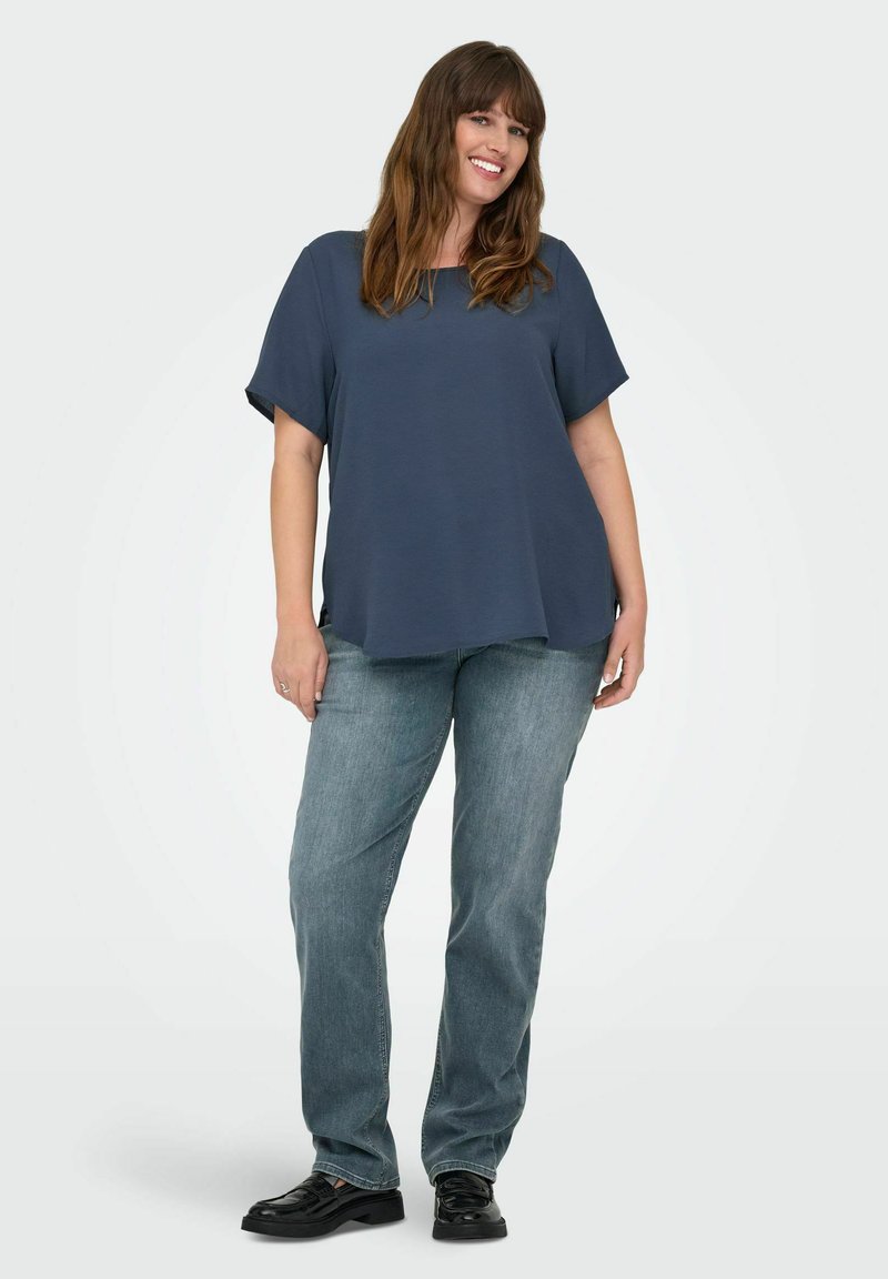 Tamno plava oversized majica kratkih rukava, u kombinaciji sa svijetloplavim ravnimfarmerkama i crnim cipelama; glatkna tkanina, opušteni kroj.