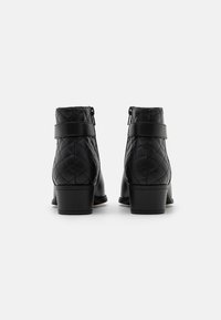 Bottines noires avec texture matelassée, présentant un bout rond, un petit talon carré et une fermeture éclair latérale, accentuées par une sangle autour de la cheville.
