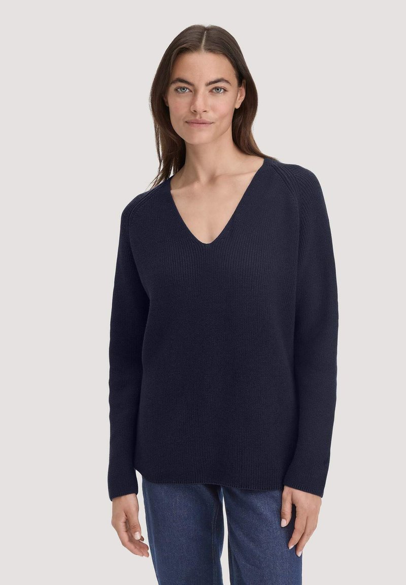 Fester marineblauer Strickpullover mit tiefem V-Ausschnitt, langen Ärmeln und gerippter Struktur, kombiniert mit Jeans. Einfaches, lässiges Design.