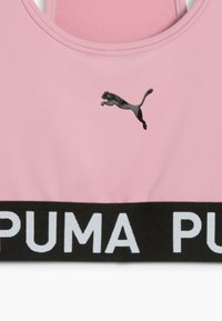 Roza športna modrček z črnim trakom, ki vsebuje 'PUMA' v belem napisu; vključuje črn mačji logotip spredaj. Gladek material z teksturiranim hrbtom.