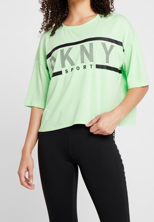 Kobieta ubrana w luźną, jasnoliściastą koszulkę DKNY Sport z czarnymi literami oraz czarne legginsy z białym napisem z boku.